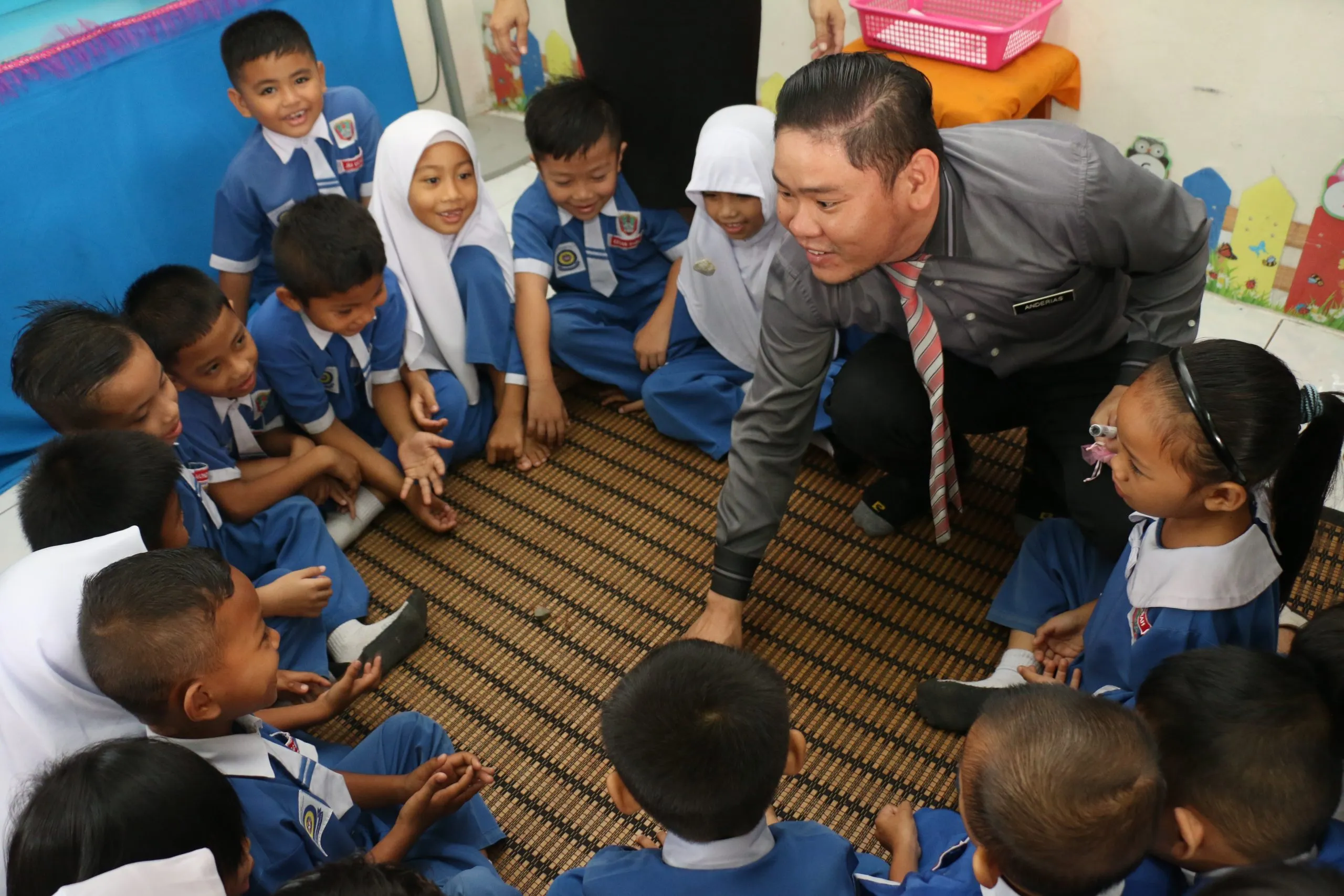 A teacher crouching to talk with pupils seated on the classroom floor