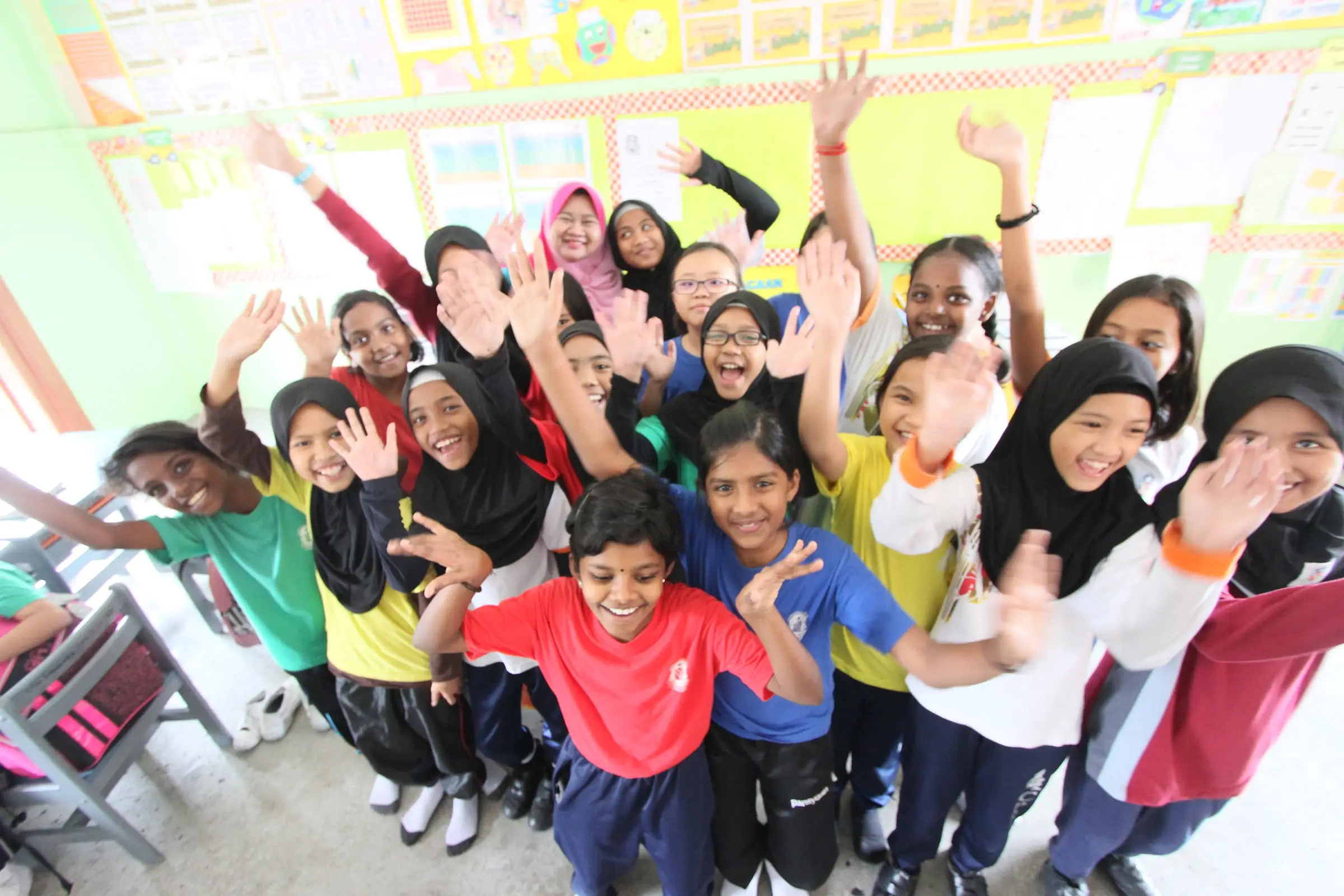 A class of primary pupils cheering with their arms raised in a brightly decorated classroom