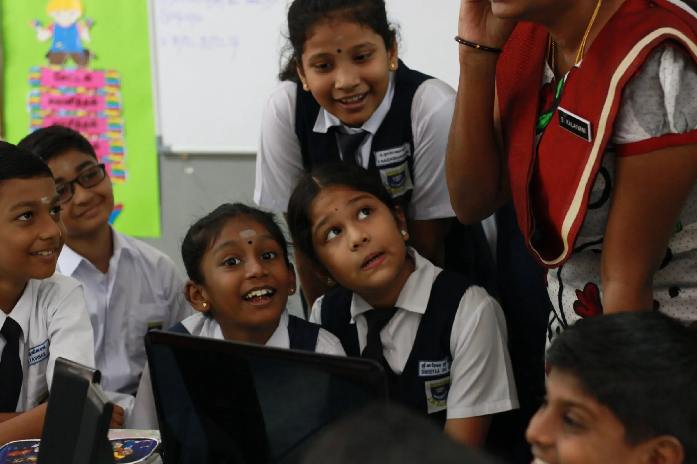 Primary pupils gathered round a laptop, one looking up and smiling