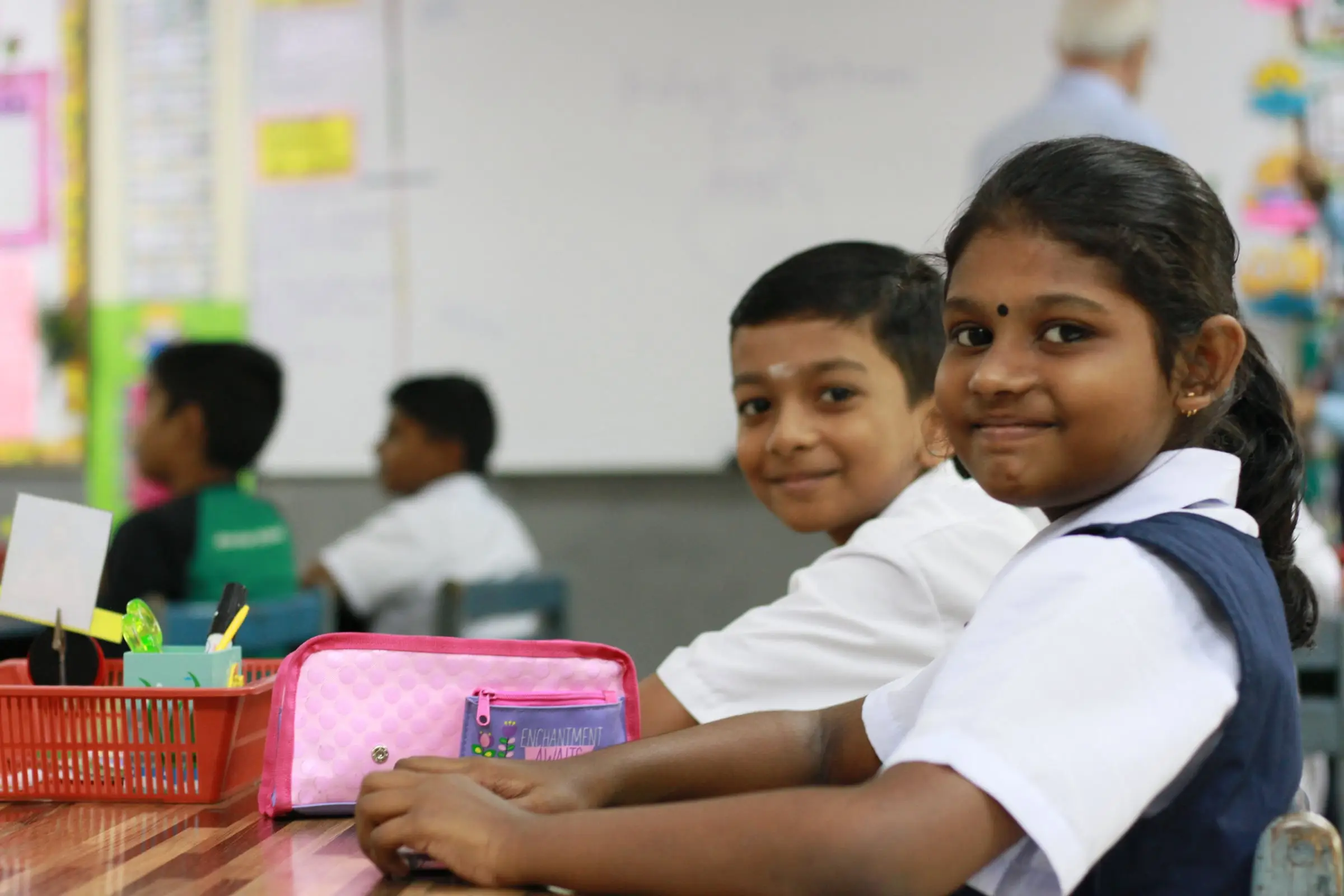 Two primary pupils at their desk turning round to smile at the camera